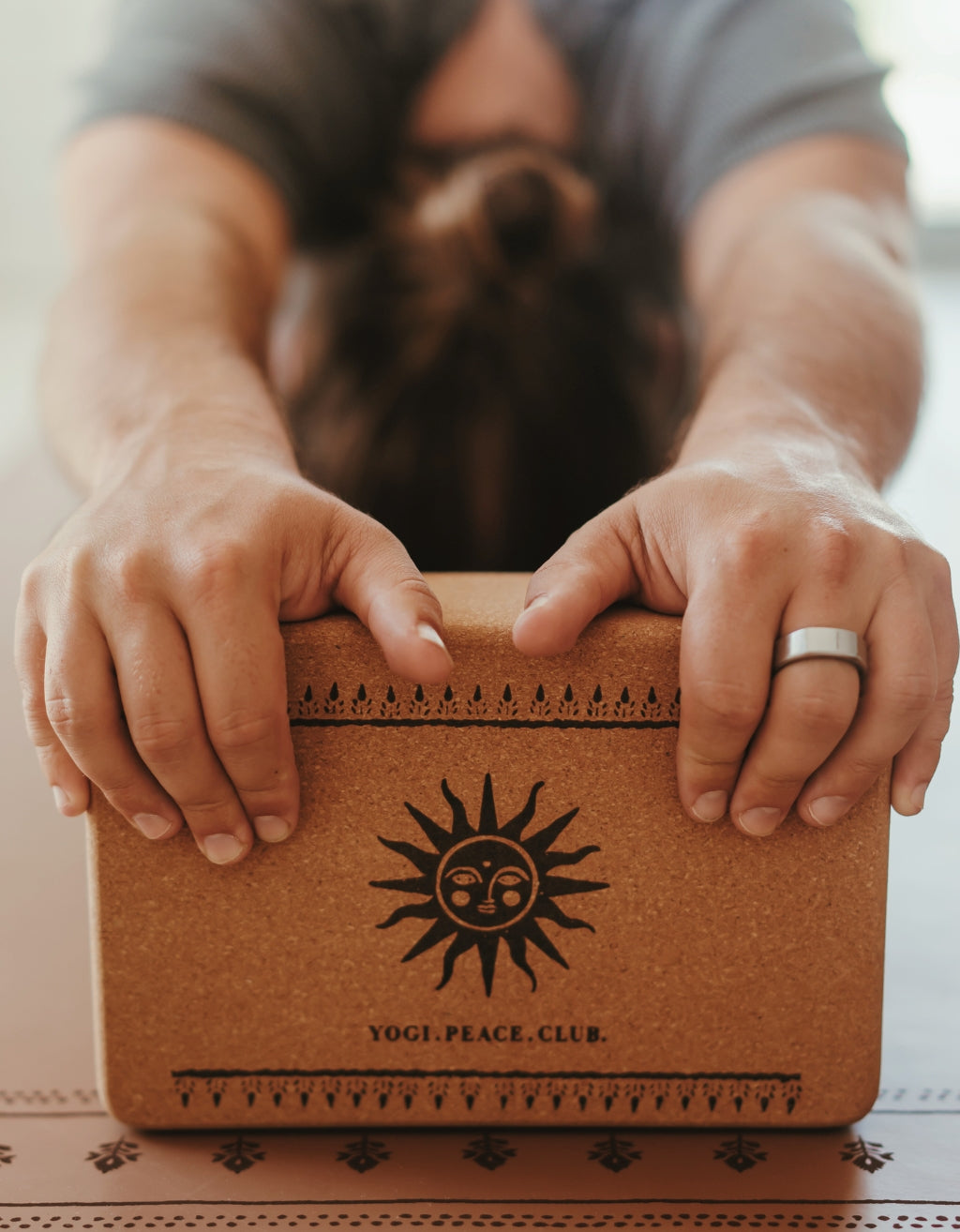 Person holding a cork yoga block with 'Yogi Peace Club' branding.